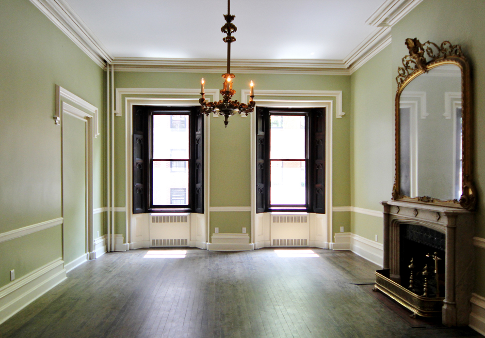 Lime-green colored empty room with two windows, a chandler, and a fireplace with a mirror above it