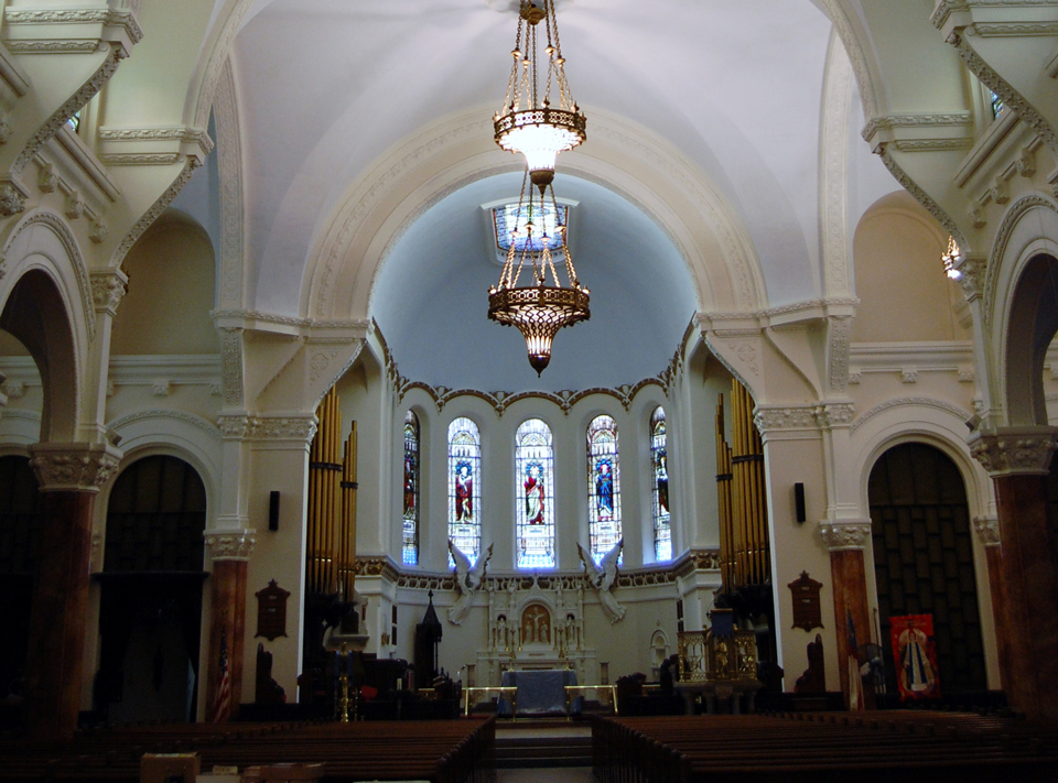 Interior center of a church with a chandler that has church pews leading up to the altar